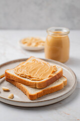 Peanut butter toast on a plate on a light marble background with nuts and knife close up.