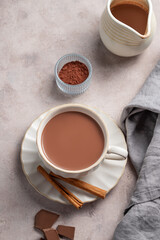 Hot chocolate in a cup on a light background with cinnamon, milk jug and napkin.