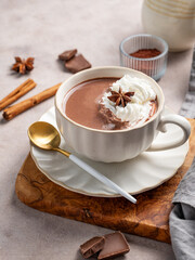 Hot chocolate in a cup with whipped cream and spices on a wooden board on a light background.