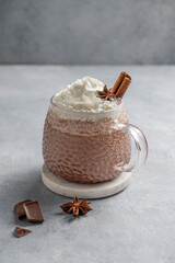 Hot chocolate in a cup with whipped cream and spices on a light background.
