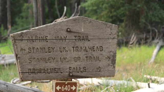 A backpacker hikes past a rustic wooden trail sign at a junction for the Alpine Way Trail, Stanley Lake Trailhead, and Bridalveil Falls in the Sawtooth wilderness of Idaho.