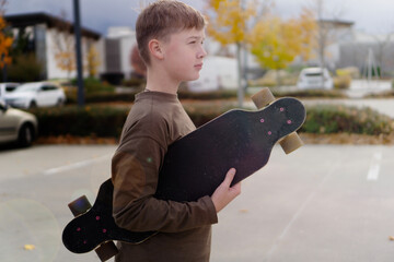 caucasian teenage boy carrying longboard under arm in empty parking lot looking away concept of youth sports, skateboarding, teen lifestyle