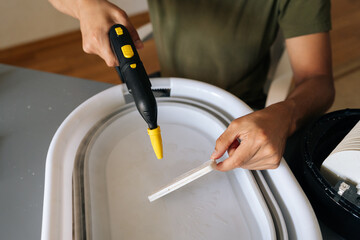 Closeup cropped shot of unrecognizable man using steam cleaner for sanitizing humidifier filter submerged in basin of water, promoting clean and healthy air for improved indoor air quality, wellness.