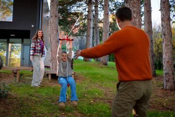 Family enjoying outdoor leisure time with a child riding a zipline in the backyard, parents watching and engaging with the boy, experiencing fun and happiness together