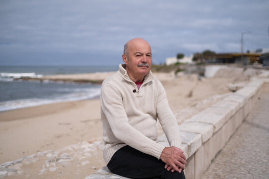 Elderly man with a mustache sitting on a seawall by the ocean  - Powered by Adobe