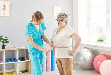 Fototapeta premium Doctor dietitian, or nurse measures the waist of an elderly patient using a tape in a healthcare clinic. Healthcare setting, measuring the waist, and patient care provided by the medical staff.