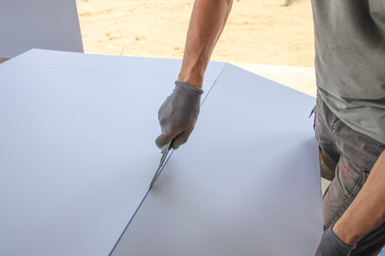 Man is cutting a piece of drywall with a utility knife