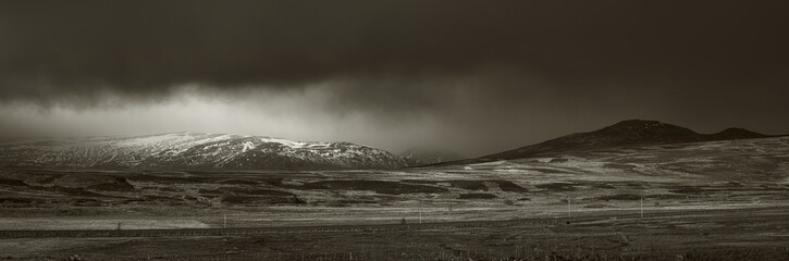Dark storm clouds over snow-capped mountains in the Scottish Highlands. Dramatic monochrome landscape with moody light.