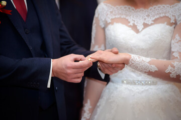 Groom putting ring on bride&rsquo;s finger. Close-up of groom placing wedding ring on bride&rsquo;s hand during ceremony