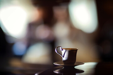 Coffee cup on table with blurred bride background. Small metallic coffee cup on reflective table with bride in background creating romantic atmosphere