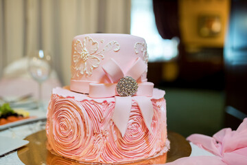 Pink wedding cake with ribbon and floral design. Elegant pink wedding cake decorated with floral pattern and bow on banquet table