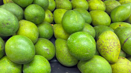 Close-up of bulk avocados (Persea americana) piled in a container for sale at a market or fair. Green fruit, some with dark spots, with a slightly rough texture.