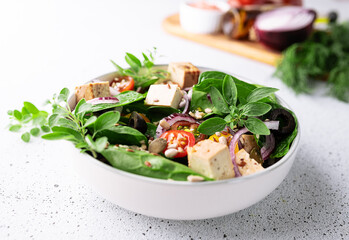 Fresh vegan salad with baby spinack leaves, tofu, cherry tomatoes, onion and seeds in ceramic bowl on white stone table top view. Healthy diet food concept.