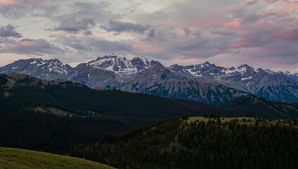 Obraz premium Mountain Peaks at Twilight, Dark Green Forest and Sky with PinkGrey Clouds.