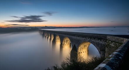 Stone viaduct shrouded in mist at dawn, illuminated by soft golden light. Dramatic, long exposure shot