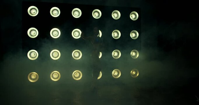 Bikini fitness competitors confidently pose on stage under bright lights demonstrating their skills in an intense competition environment. The atmosphere is enhanced by low fog and striking visuals.