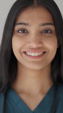 Vertical video. Close-up portrait of a confident and friendly young indian healthcare professional in scrubs and a stethoscope, looking directly at the camera with a warm smile