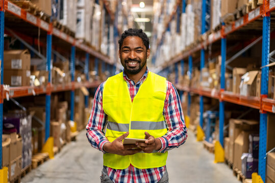 Warehouse worker smiling while holding a tablet in a large distribution center - Powered by Adobe