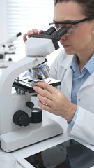 Female scientist wearing protective gear analyzing test samples under microscope in contemporary research environment. Medicine, healthcare and science concept