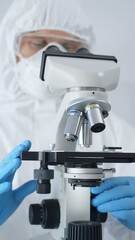 Male scientist virologist wearing hazmat suit, mask, and blue gloves, diligently working at a microscope in a laboratory researching viruses. Medicine and science concept