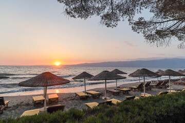 Beautiful sandy beach with parasols and sun loungers on the Turkish Aegean coast near Izmir and the Greek islands in the Mediterranean Sea in the evening sun in summer, Turkey Europe and Asia