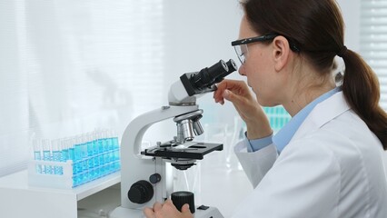 Female scientist examining microscope slide, analyzing chemical sample in sterile laboratory...