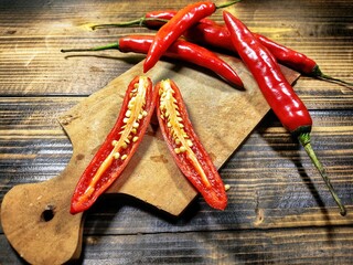 A red chili pepper is sliced open, revealing its seeds and membrane on a wooden cutting board, with...