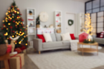 Interior of festive living room with grey sofa, glowing Christmas tree and table, blurred view