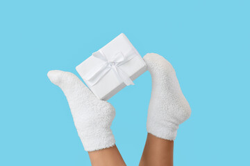 Legs of young woman with Christmas gift box on blue background