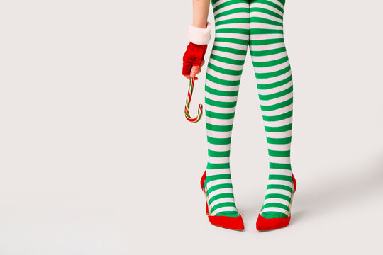 Young woman in striped stockings with candy cane on grey background. Christmas celebration