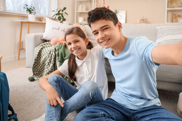 Happy brother and sister taking selfie while sitting on floor in living room