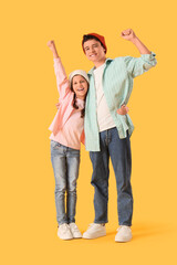 Happy brother and sister in hats with raised hands on yellow background