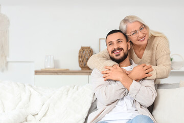 Fototapeta premium Mature woman hugging her son on sofa at home