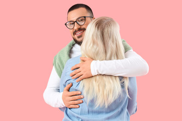 Young man hugging his mother on pink background