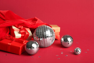 Santa bag, disco balls, Christmas gift boxes and confetti on red background, closeup