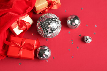 Santa bag, disco balls, Christmas gift boxes and confetti on red background, closeup