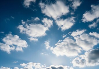 A high-resolution photograph of a bright blue sky filled with soft, fluffy cumulus clouds. The clouds appear voluminous and scattered across the horizon, illuminated by natural sunlight. Captured from