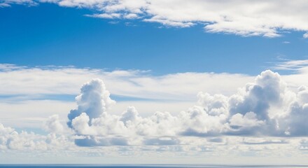 A high-resolution photograph of a bright blue sky filled with soft, fluffy cumulus clouds. The clouds appear voluminous and scattered across the horizon, illuminated by natural sunlight. Captured from