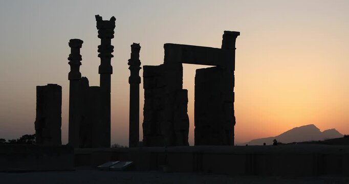 Silhouetted Achaemenid columns and ruined walls at Persepolis as the sun dips behind the Zagros mountains. Quiet desert dusk&mdash;heritage, endurance, and the passing of empires.