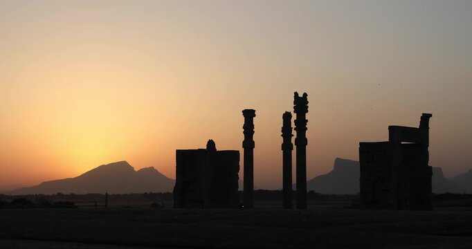 Silhouetted Achaemenid columns and ruined walls at Persepolis as the sun dips behind the Zagros mountains. Quiet desert dusk&mdash;heritage, endurance, and the passing of empires.