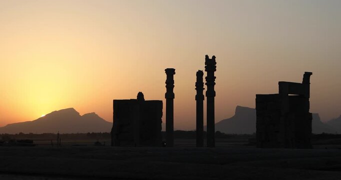 Silhouetted Achaemenid columns and ruined walls at Persepolis as the sun dips behind the Zagros mountains. Quiet desert dusk&mdash;heritage, endurance, and the passing of empires.