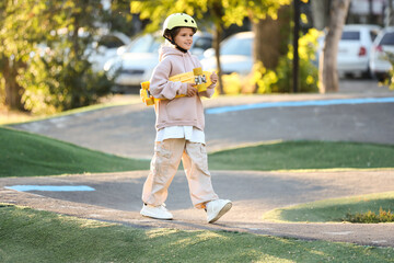 Little girl with helmet and skateboard walking in park