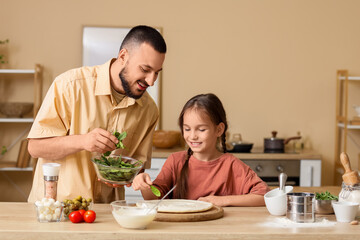 Father with his daughter putting spinach to pizza dough in kitchen