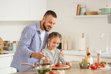 Father with his daughter applying tomato sauce to pizza dough at table in kitchen