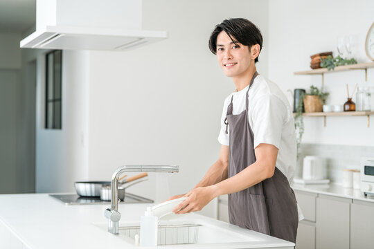 Young Asian man in an apron washing dishes in the kitchen
 - Powered by Adobe