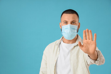 Young man in medical mask showing stop gesture on blue background