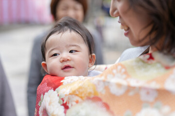 A woman is holding a baby in her arms. The baby is smiling and looking at the camera. The woman is...