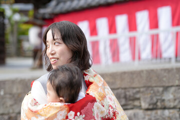 Fototapeta premium A woman is holding a baby in a red and orange cloth. The baby is smiling and the woman is smiling back. The scene is warm and happy, with the woman and baby enjoying each other's company