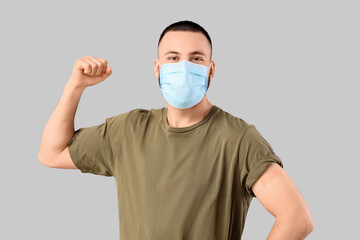 Young man in medical mask with applied medical patch showing muscles on grey background