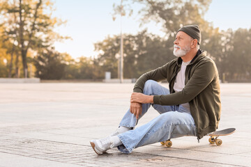 Senior man with skateboard sitting on city street